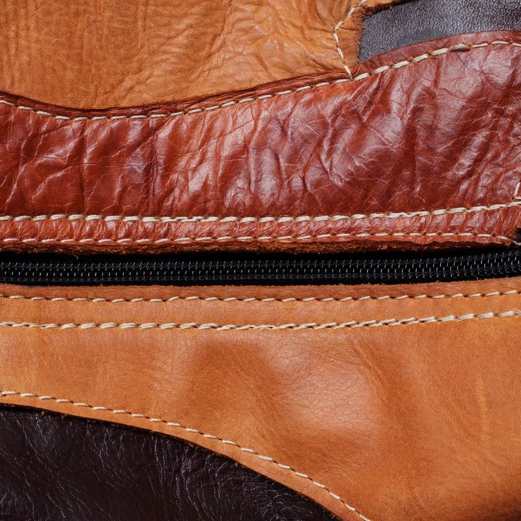 Close-up image of a section of a leather item showing different textures and colors of top grain buffalo leather, including smooth, wrinkled, and creased areas with visible stitching and a zipper.