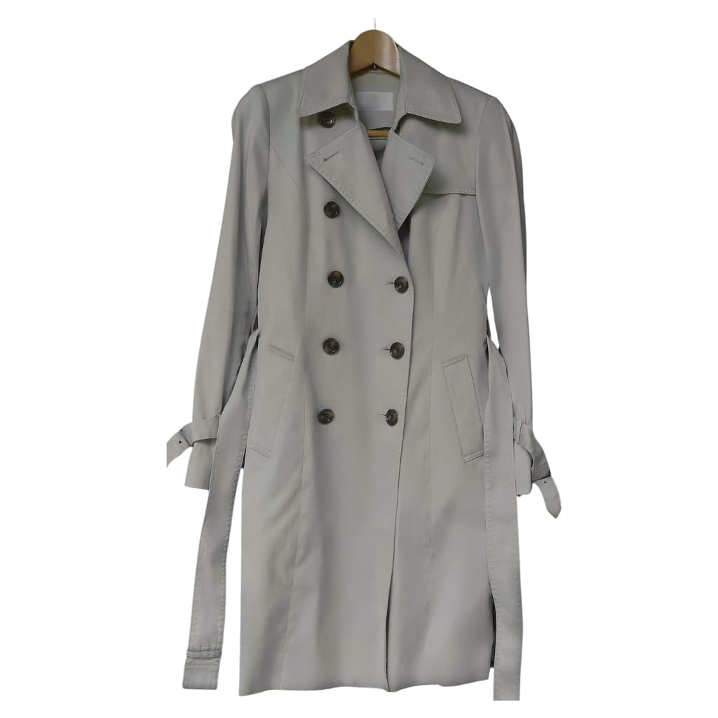 A classic light gray trench coat hanging on a wooden hanger against a plain white background.

