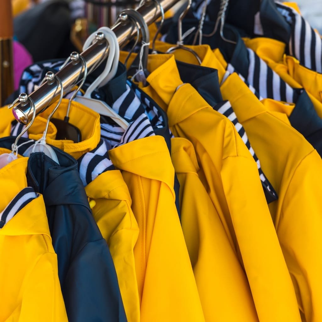 A display of yellow and striped rain jackets hanging on a metal clothing rack, highlighting the hoods.