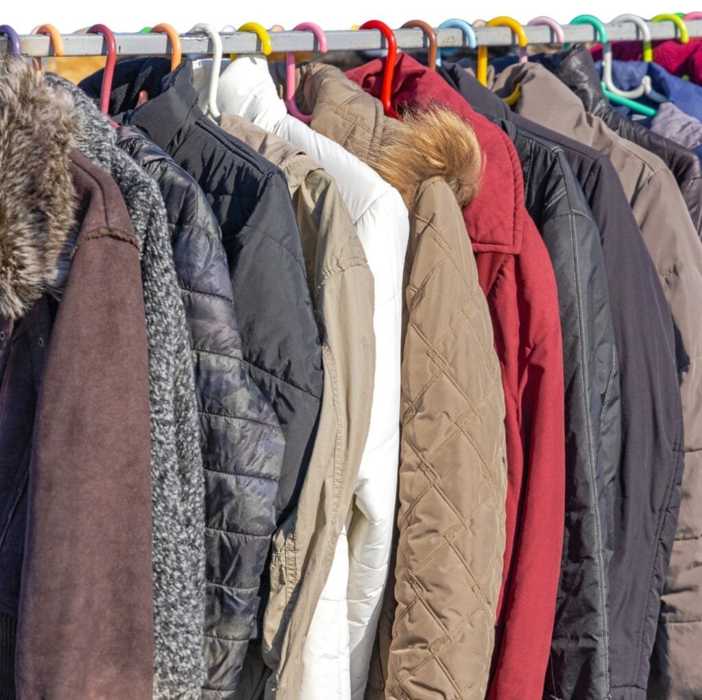 A row of various winter jackets and parkas hanging on a colorful clothing rack, featuring different colors, styles, and sizes suitable for all ages.