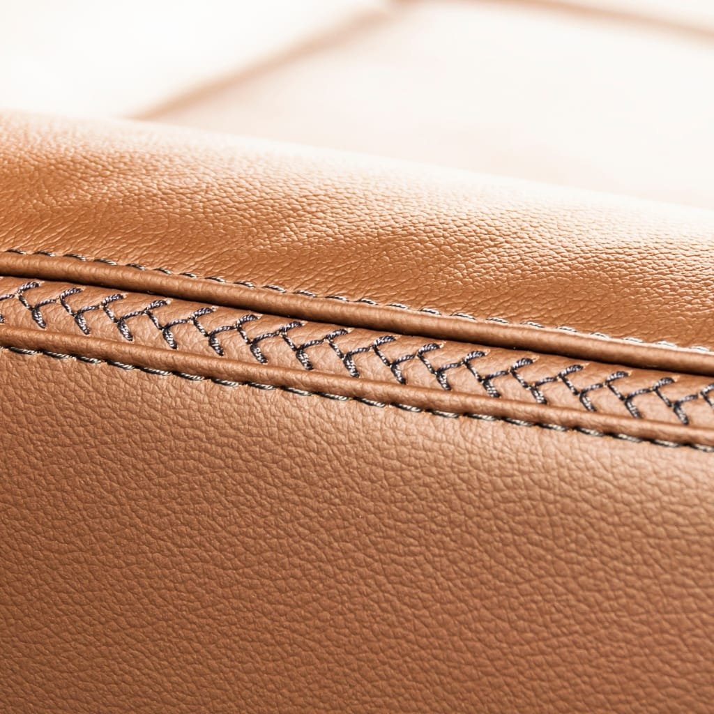 A close-up of tan-colored leather material showing detailed stitching and textured surface.


