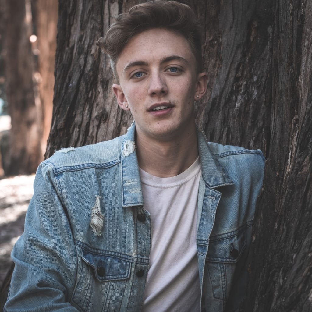 Man wearing a lightweight denim trucker jacket over a white t-shirt during a summer evening.

