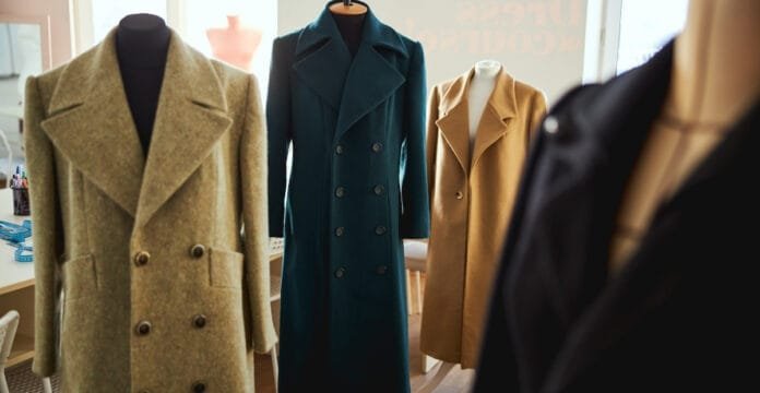 A display of four wool coats on mannequins, featuring various styles in different colors and cuts.