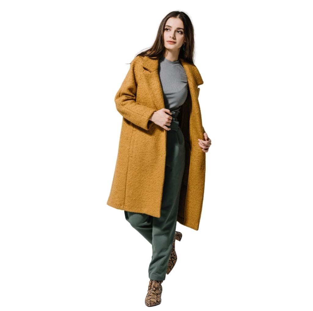 A woman wearing a long, mustard-colored wool coat over a gray top and dark green pants, standing against a white background.