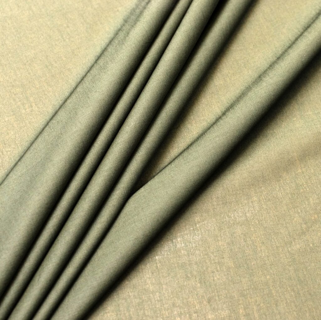 Close-up view of soft, pale green cambric linen fabric with gentle pleats running diagonally across the surface.