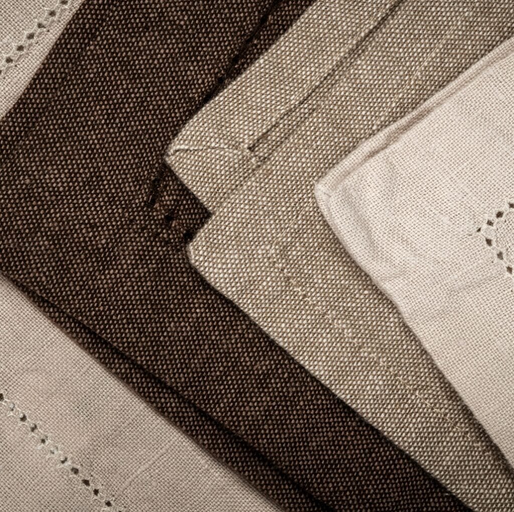 Close-up image of layered linen fabric in shades of beige and brown, showing detailed woven texture.