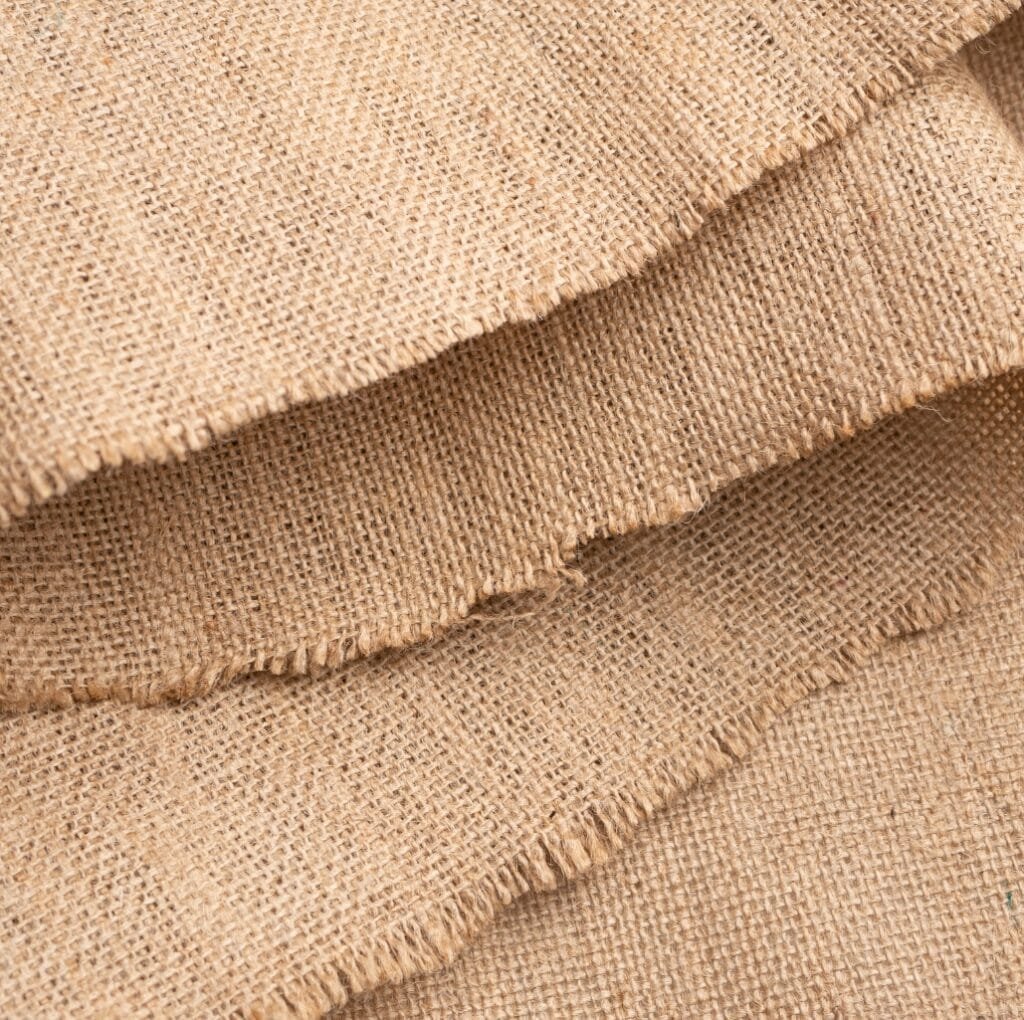 Close-up of coarse, natural beige linen fabric with a rough, open weave and visible slub texture.