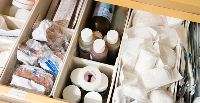 A medical drawer opened to reveal organized compartments with cotton balls, gauze pads, and assorted medical supplies such as bottles, wrapped items, and bandages.