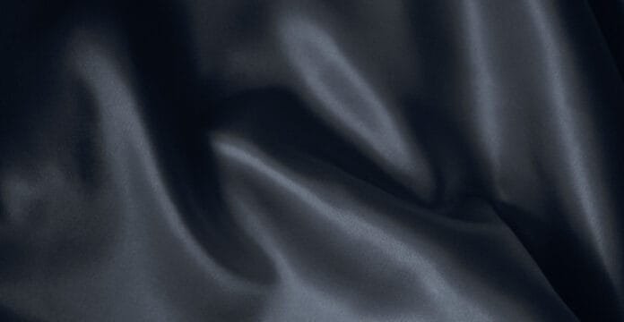 A close-up view of dark blue linen fabric with soft, flowing folds and gentle sheen.