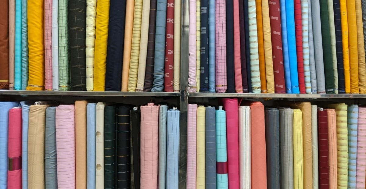 How to Cool and Cut Polyester Fabric for Best Results A colorful assortment of rolled fabrics arranged on shelves, featuring a wide range of colors and patterns including yellows, blues, pinks, greens, and neutrals in vertically standing rolls.