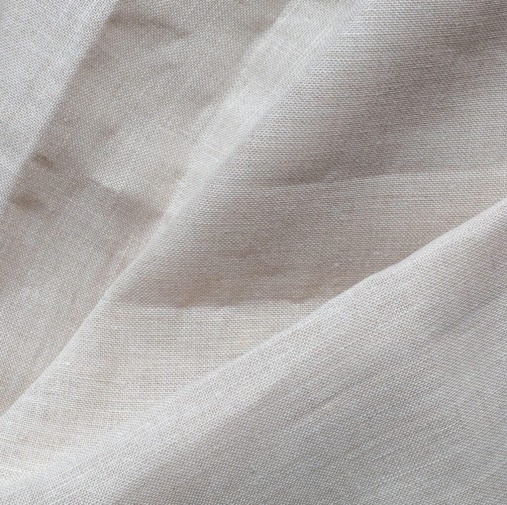Close-up view of light, natural-colored Irish linen fabric with visible weave and soft drape, showing gentle folds and texture.