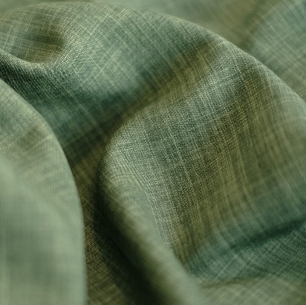 Close-up photo of a soft, green linen blend fabric with a subtle crosshatch weave and gentle folds.