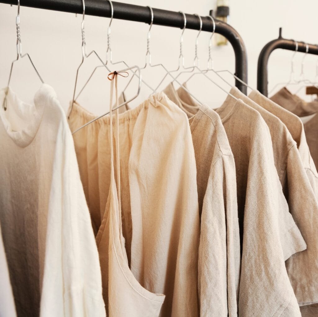 A row of linen garments hanging on a clothing rack in neutral beige and cream tones, showing lightweight fabrics and natural textures.