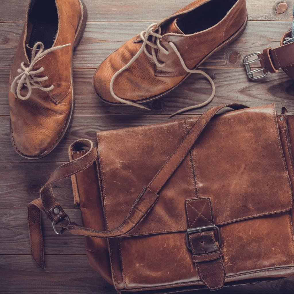 A pair of brown leather shoes and a matching brown leather messenger bag laid on a wooden surface.