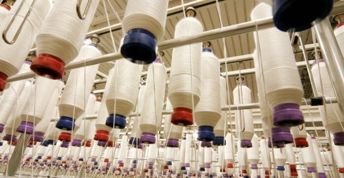 A textile factory spinning room with many large white cones of thread suspended from above, each with colored caps and threads trailing