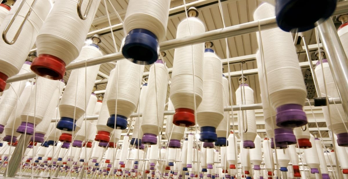 Process of Spinning Polyester: Turning Threads into Textiles A textile factory spinning room with many large white cones of thread suspended from above, each with colored caps and threads trailing