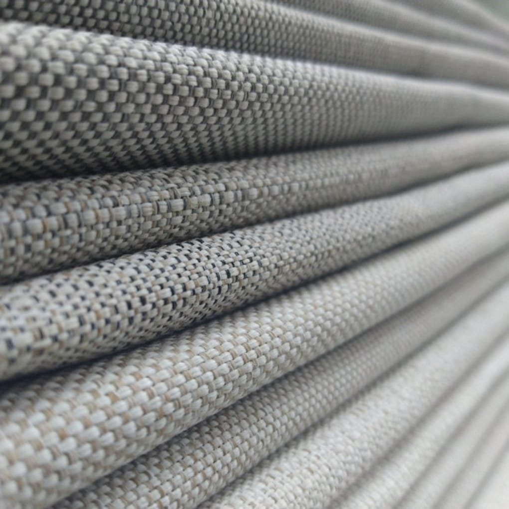 Close-up of stacked woven fabrics in neutral beige and gray tones, showing tight, textured weaves and subtle pattern variations.