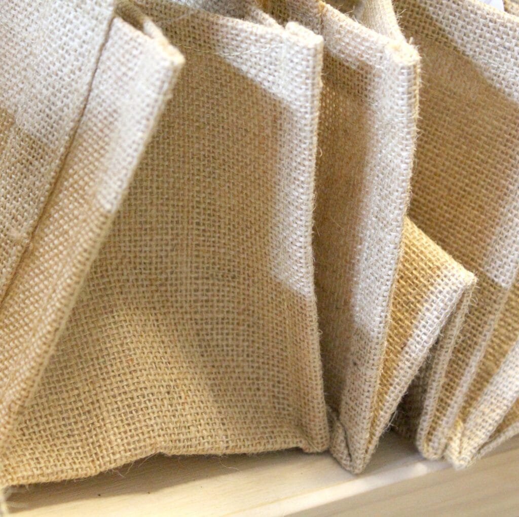 A close-up view of several folded burlap-like linen blocks standing upright on a wooden surface, showing the coarse, woven texture of huckaback fabric.