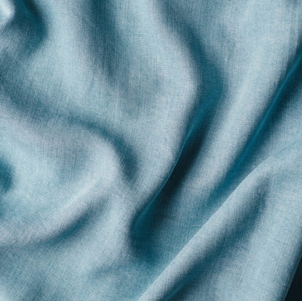 Close-up of light blue linen fabric showing natural folds and soft texture.
