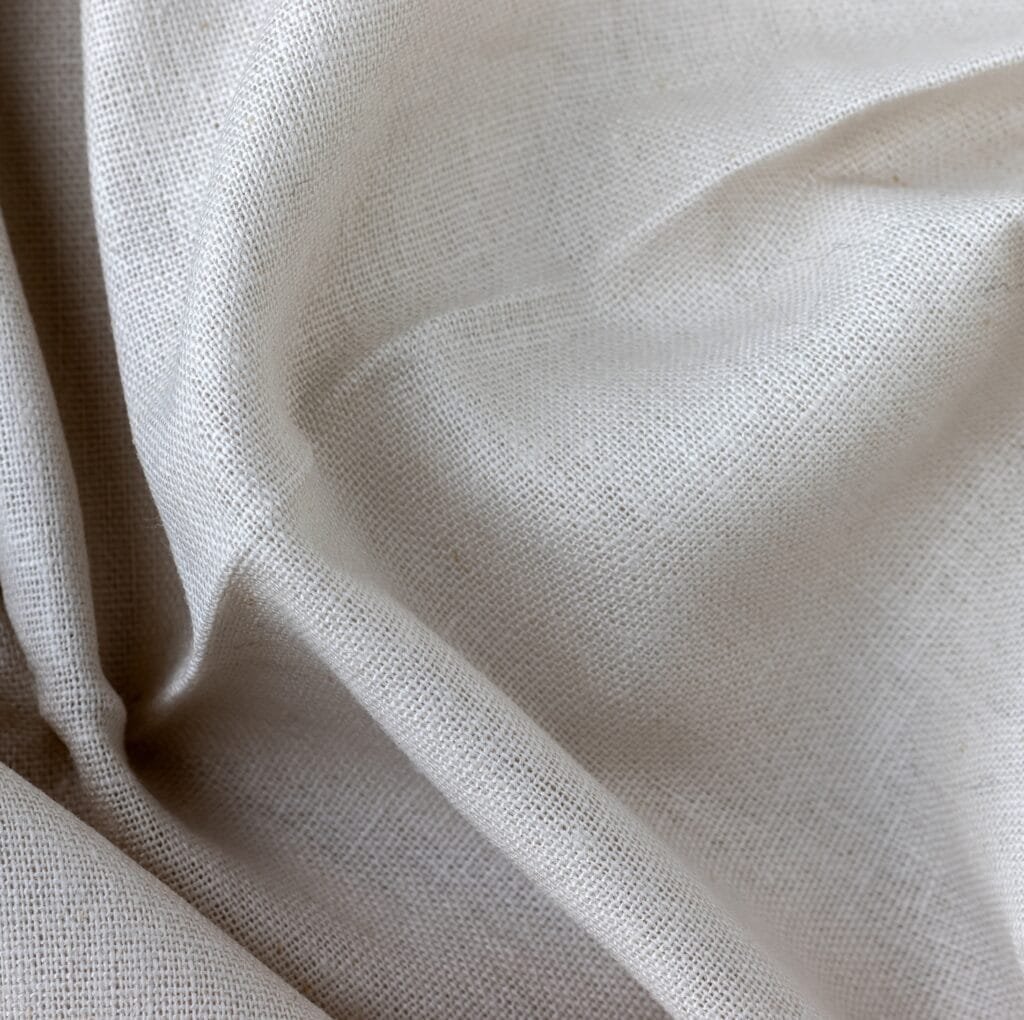 A close-up shot of light beige linen fabric with a natural, textured weave and soft folds.