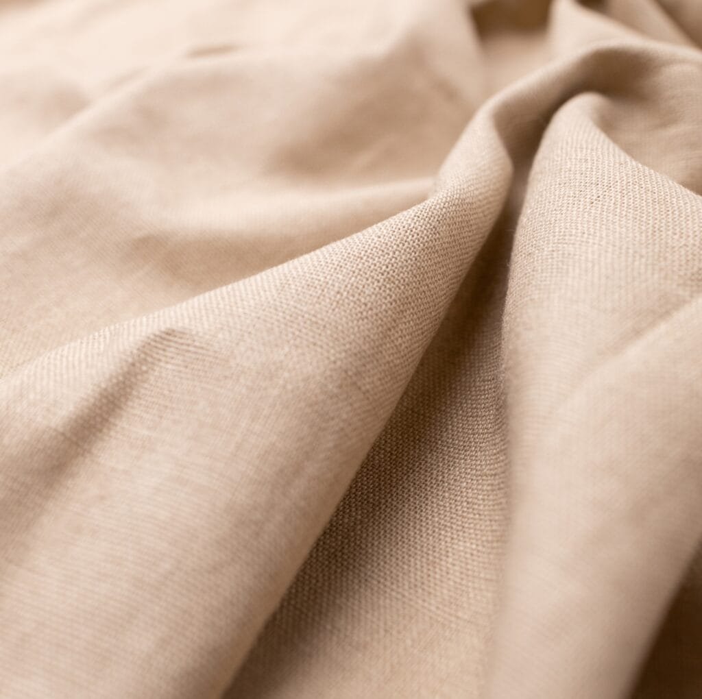A close-up of beige blended linen fabric, showing soft folds and a slightly textured weave.