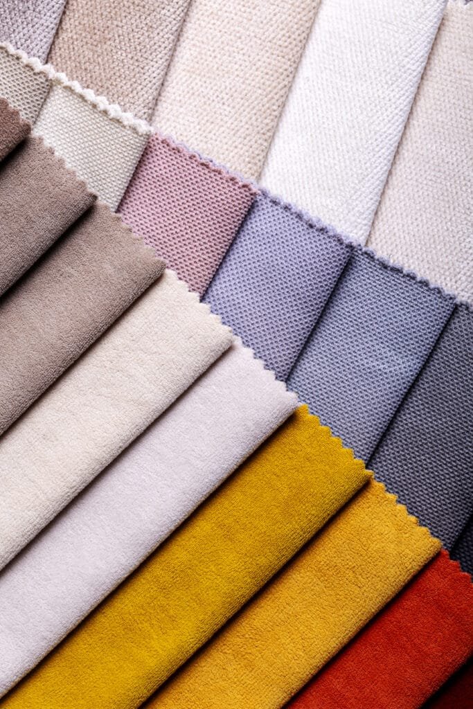 A collection of fabric swatches showcasing various colors and textures, primarily in soft, neutral, pastel, and vibrant hues, arranged in diagonal layers.