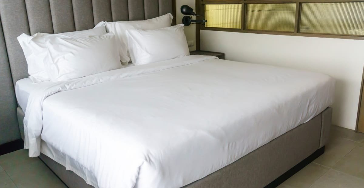 A neatly made bed with white cotton sheets and pillows in a modern hotel-style room.