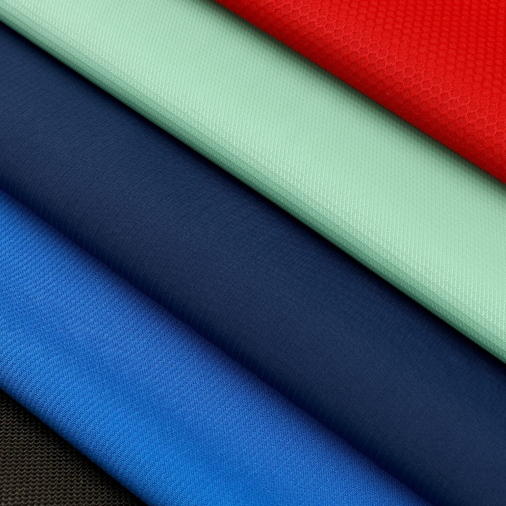 A stack of colorful fabric rolls arranged diagonally: red, mint green, light blue-green, navy, royal blue, and dark brown/black at the bottom. Each fabric has a smooth, finely textured weave.