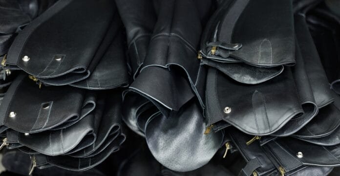 Stacks of black buffalo leather bags or pouches with zippers and metal snaps, piled together.