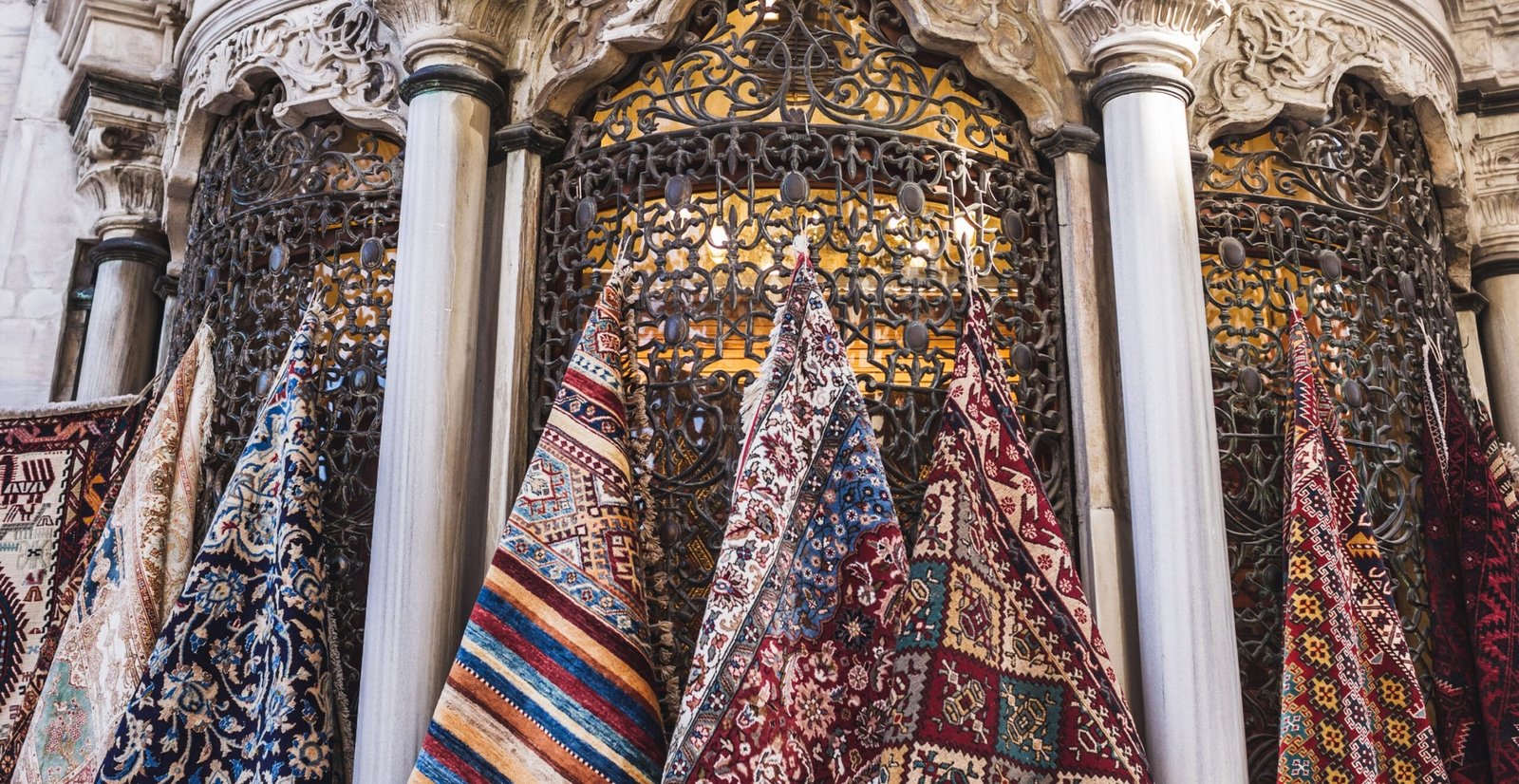 Venice Linen Fabric: Luxury, Durability, and Timeless Style “A row of colorful woven rugs hanging along ornate ironwork and marble columns in a decorative storefront.” Venice Linen Fabric
