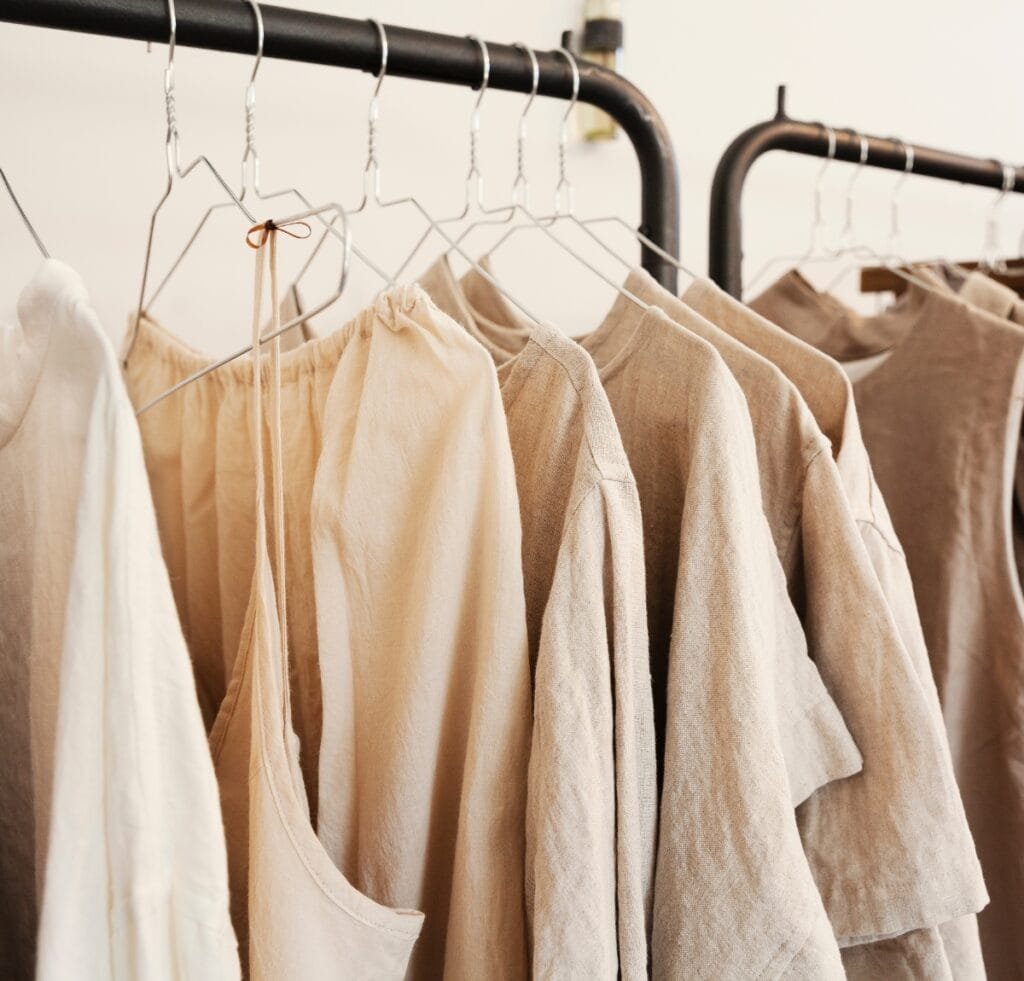 "A row of light to medium brown linen garments hanging on metal clothes racks, displaying soft, natural textures and neutral tones."