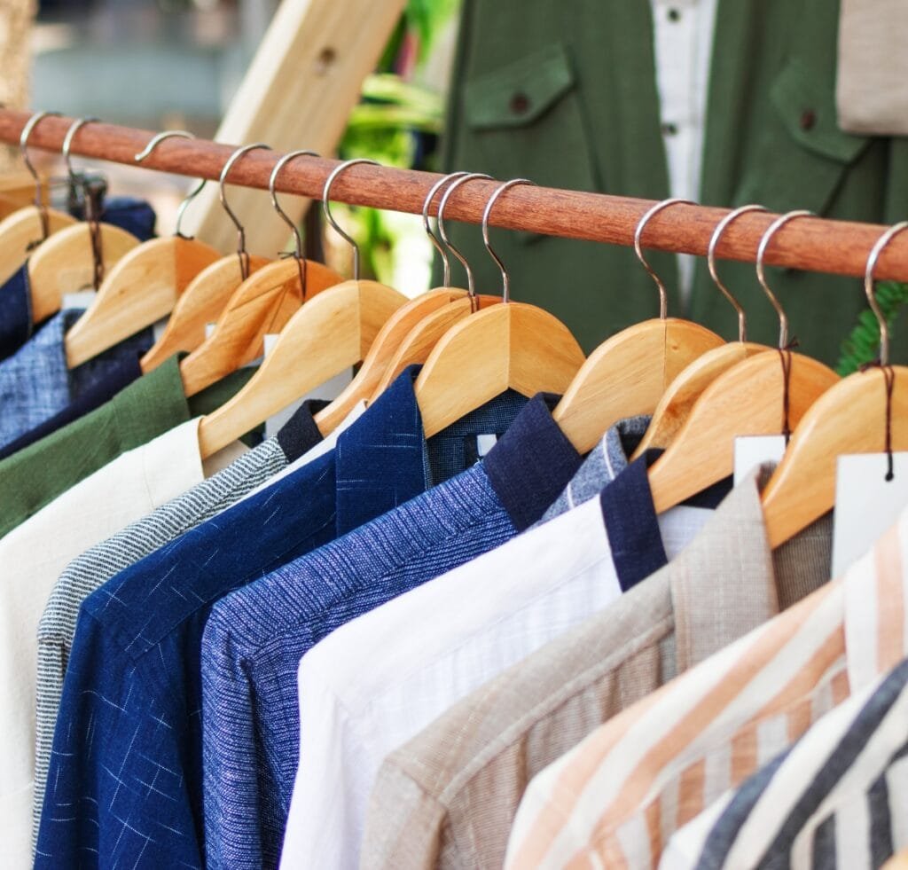 A row of men's shirts on wooden hangers hanging on a rod in a clothing store, showcasing a variety of light to medium-weight fabrics, including linen textures. Hebei Linen Fabric