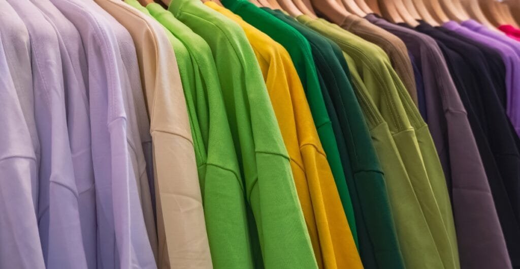 "Row of colorful sweatshirts on hangers arranged in a rainbow spectrum."
