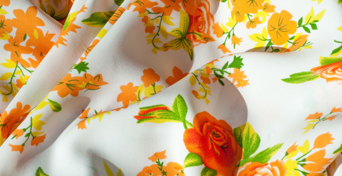 White fabric with bright orange and yellow floral pattern, showing folded and draped sections.