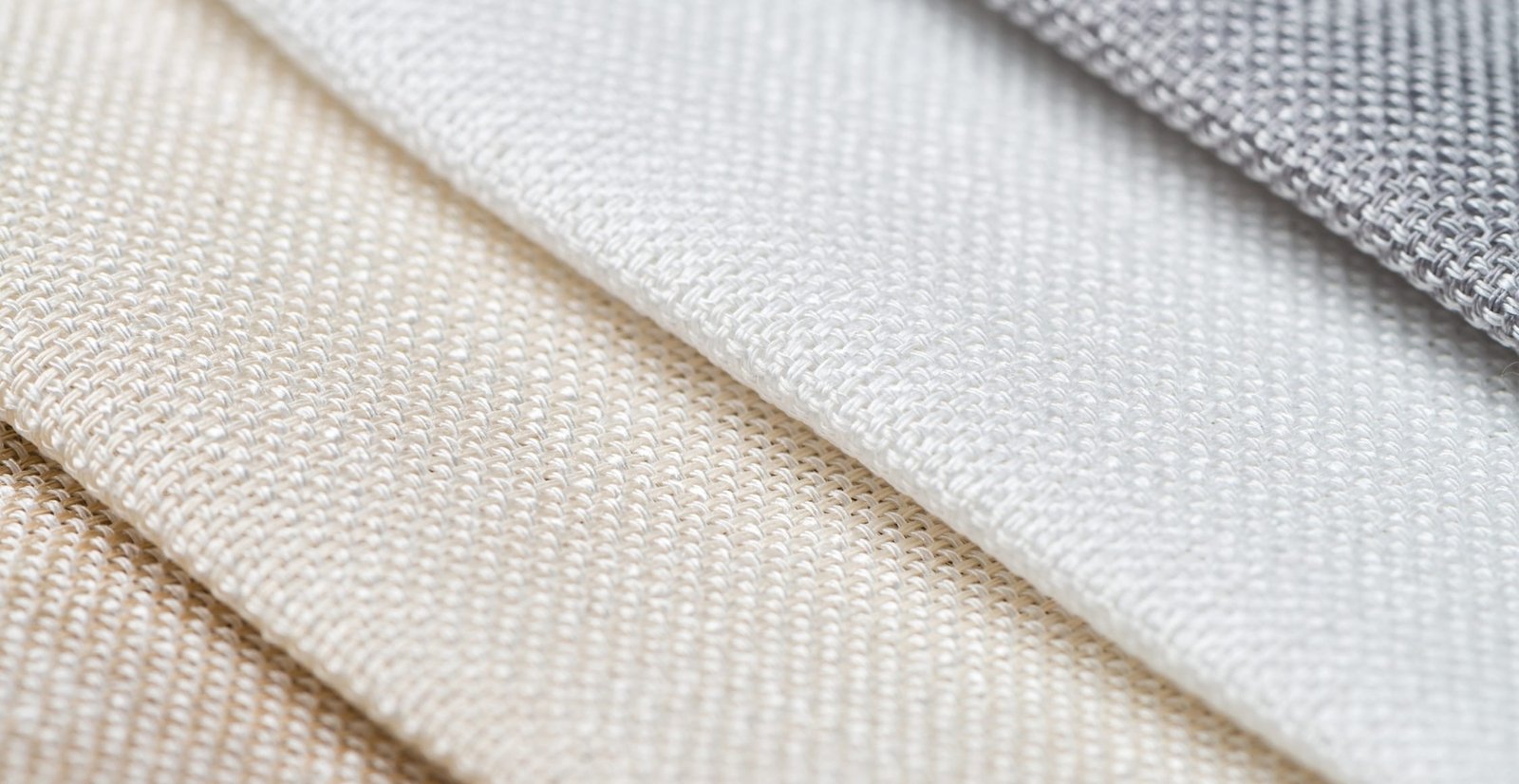 A close-up view of textured bird’s eye linen fabric in soft neutral tones, showing the tiny woven pattern and subtle ridges across the folded textile.