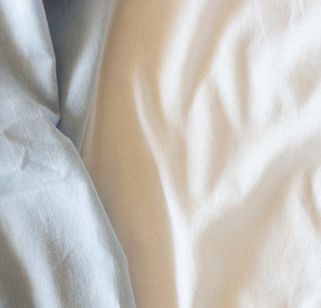 Close-up of soft, light-colored blended linen fabric with gentle folds and subtle texture.
