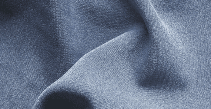 A close-up of soft, light-blue fabric with gentle folds and smooth texture.