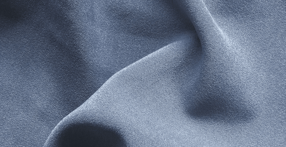 A close-up of soft, light-blue fabric with gentle folds and smooth texture.
