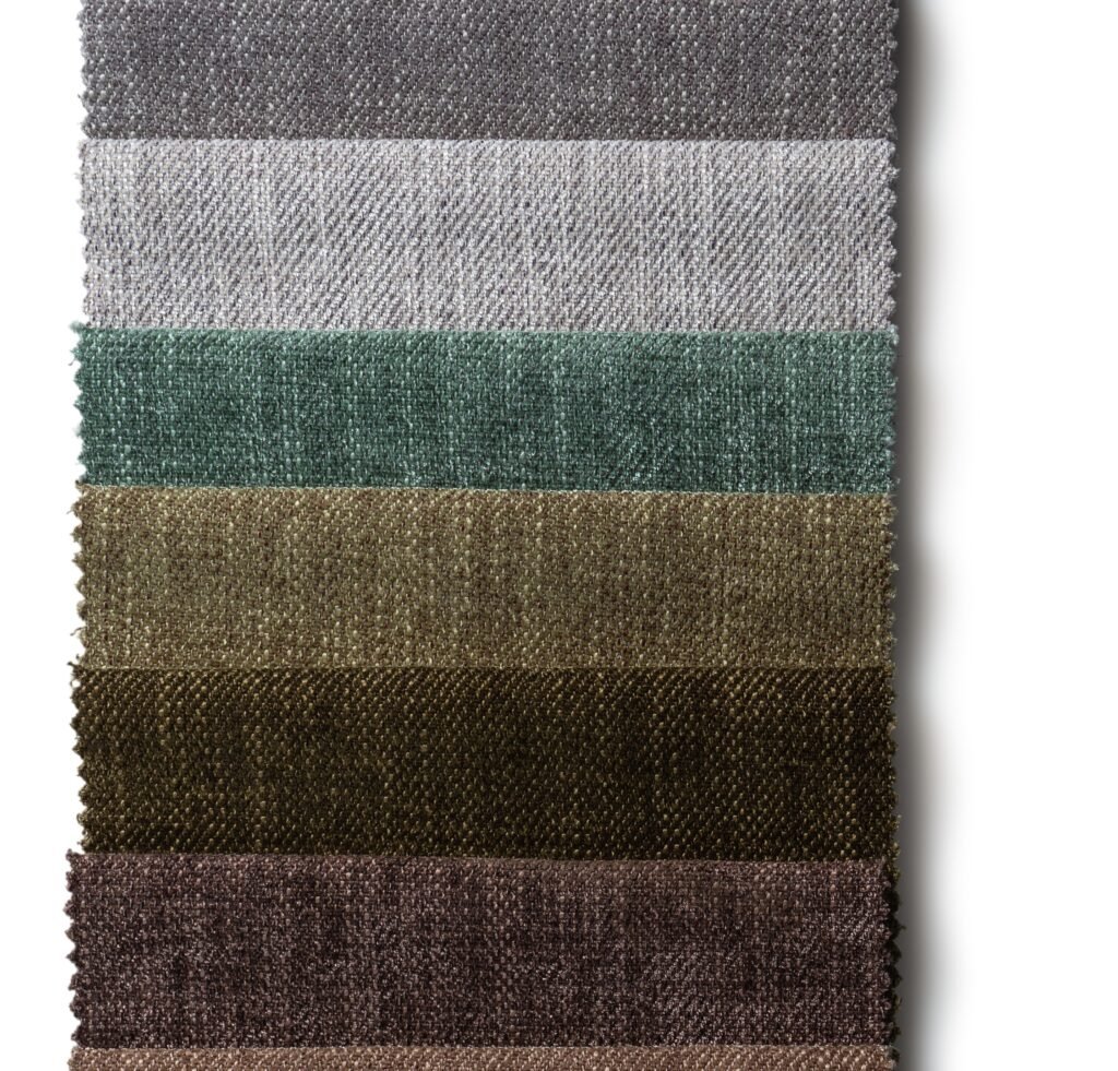 A vertical stack of woven fabric swatches in rich earth tones, from top to bottom: dark gray, light gray, muted teal, olive green, warm tan, chestnut brown, and deep brown, each with a textured linen-weave surface and pinked edges.