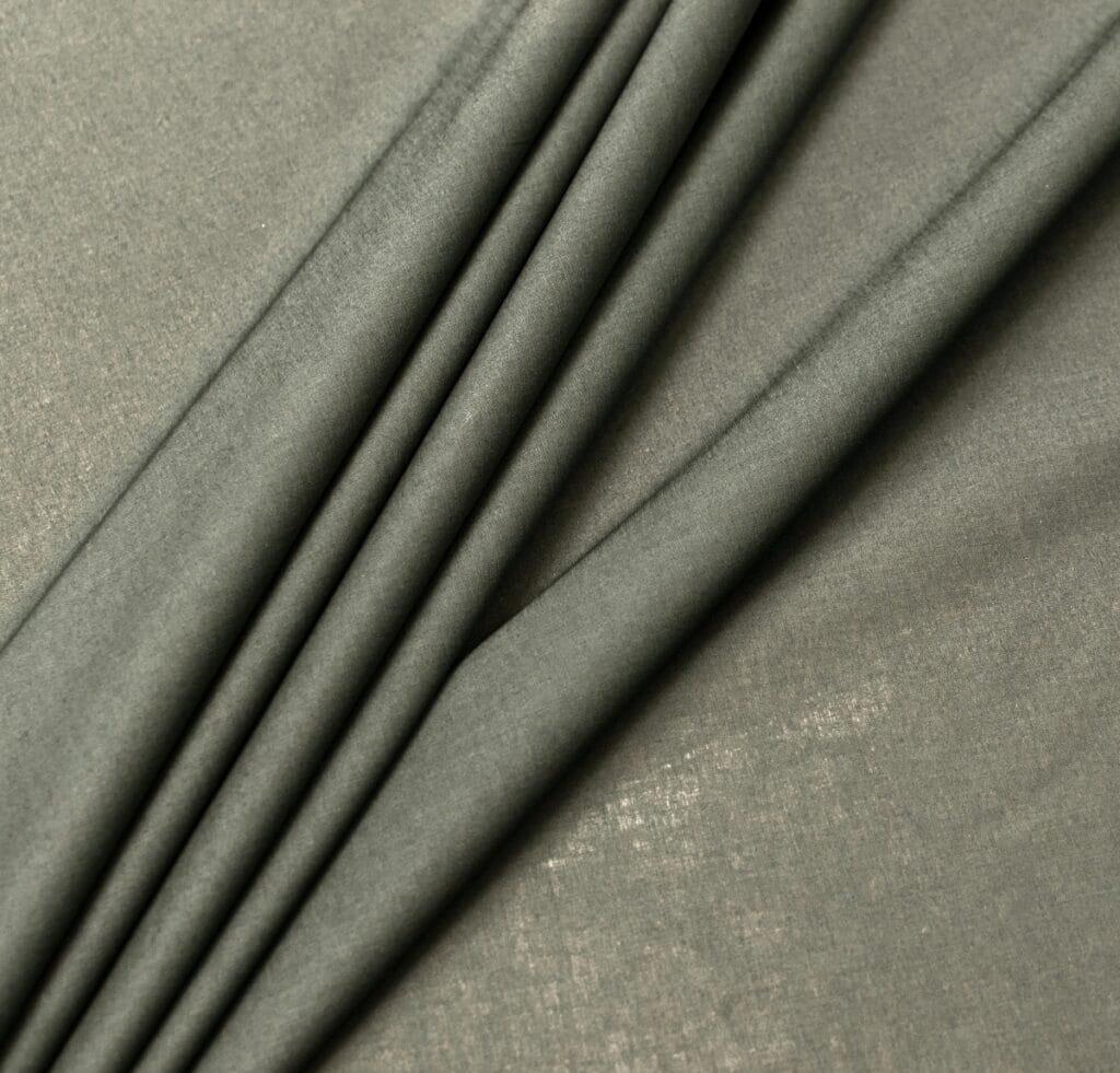 “Close-up of soft, finely woven cambric linen fabric in a muted olive-gray color with gentle folds and a subtle sheen.”