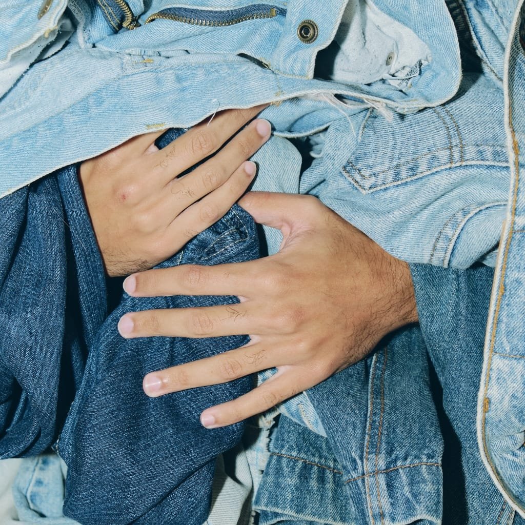 Two people wearing blue denim jeans and jackets with one person’s hand resting on the other's leg and chest, showing close interaction and protective touch.
