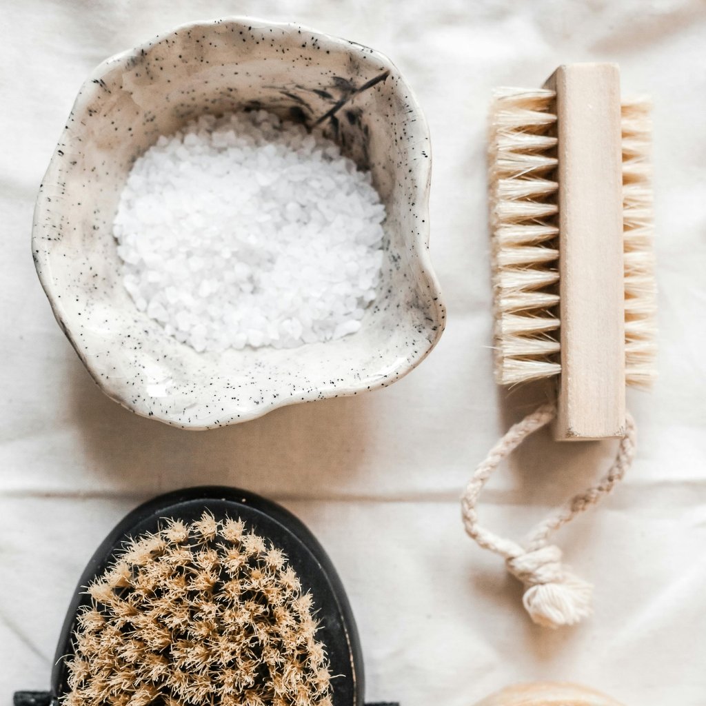 Close-up of a crushed organza fabric item with a soft, translucent texture, photographed alongside a wooden cleaning brush and a marble-patterned ceramic bowl filled with coarse salt.