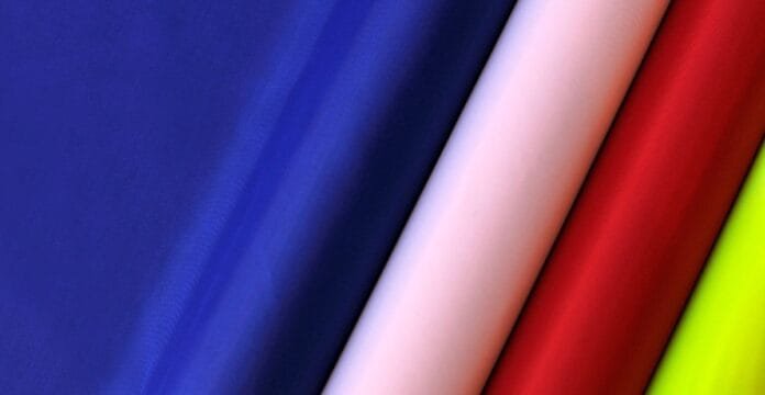 Diagonal close-up of folded colorful fabrics in royal blue, light pink, red, and lime green, showing smooth polyester material.