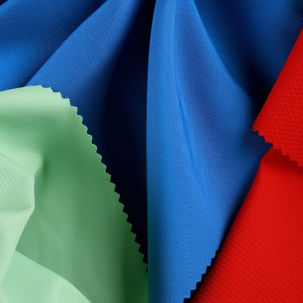 Cationic Dyeable Polyester – Properties, Benefits & Uses 5 Swatches of cationic dyeable polyester fabric in blue, light green, and red, with a textured weave and serrated edges visible.