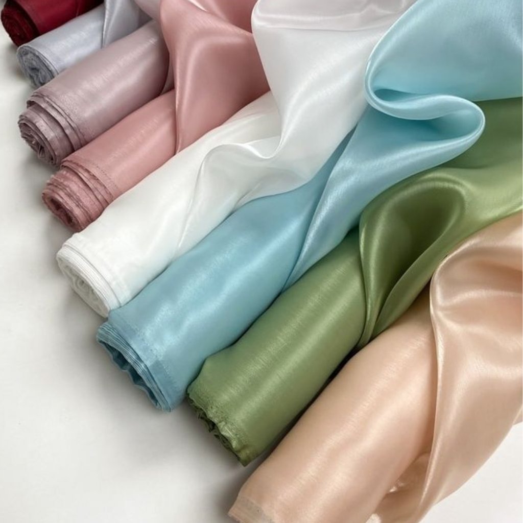 Rolled swatches of silky satin fabric in various colors, including burgundy, pink, white, light blue, green, and beige.