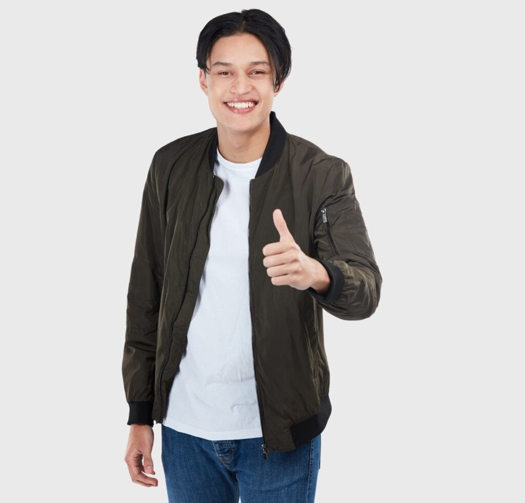 Flight Bomber Jacket: Timeless Style Meets Modern Utility 5 “Young man wearing a dark olive bomber jacket over a white t-shirt and blue jeans, smiling and giving a thumbs-up against a light gray background.”