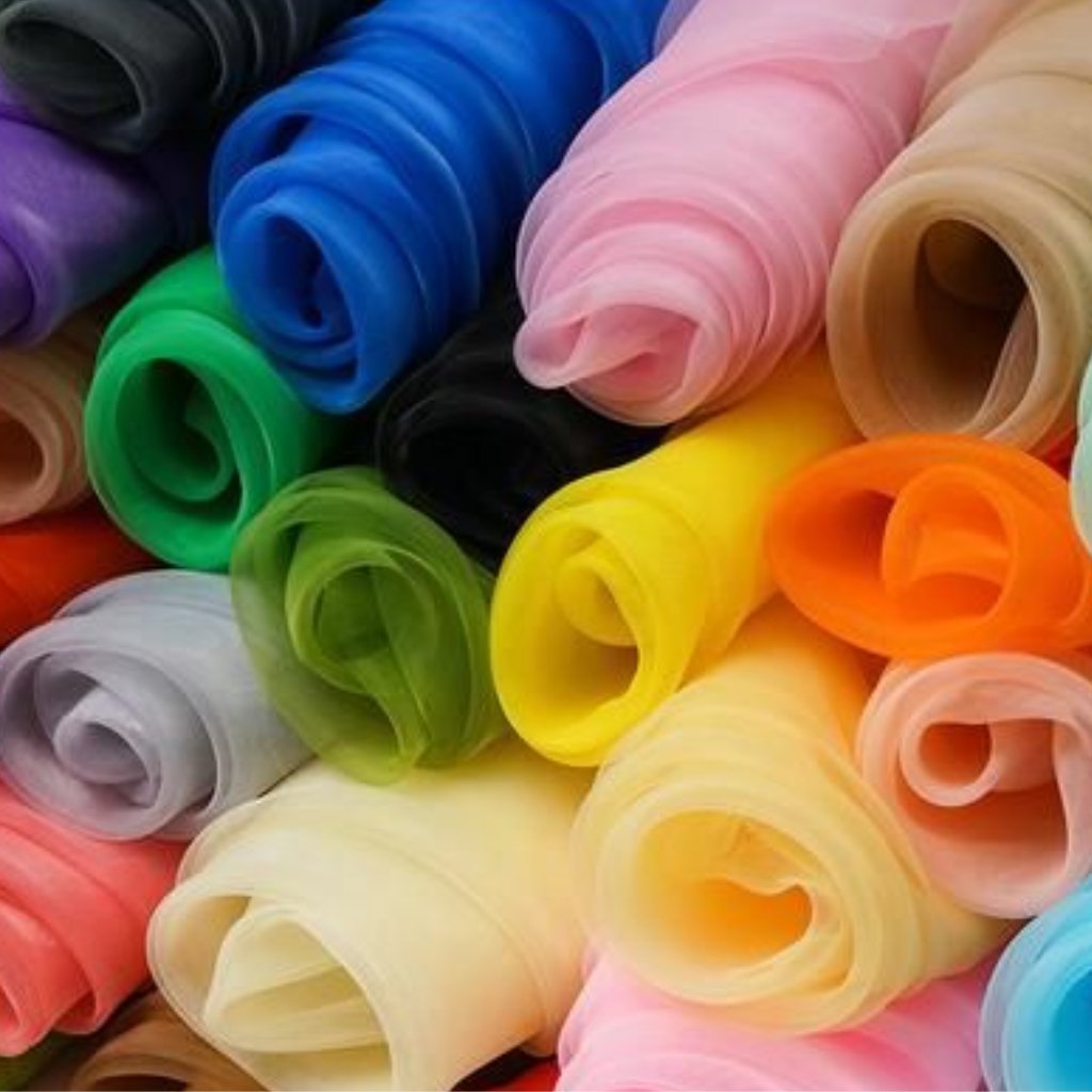 A close-up collage of rolled polyester organza fabric in a vibrant rainbow of colors, including blue, green, pink, purple, yellow, orange, and peach. Each roll shows sheer, delicate, and slightly crinkled edges characteristic of organza, with light-catching highlights.
