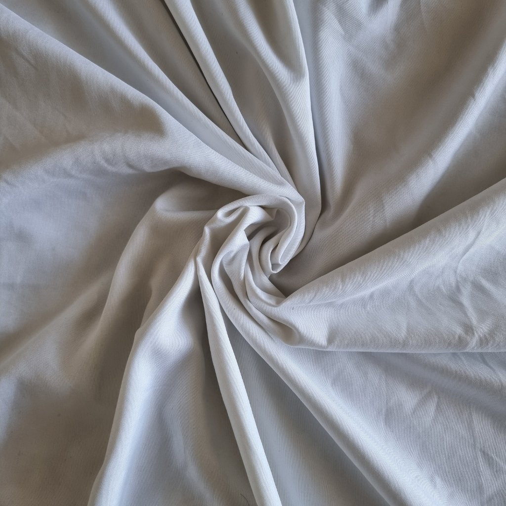 A close-up image of soft, white cotton voile fabric twisted into a spiral, showing smooth, lightweight drape and gentle folds.