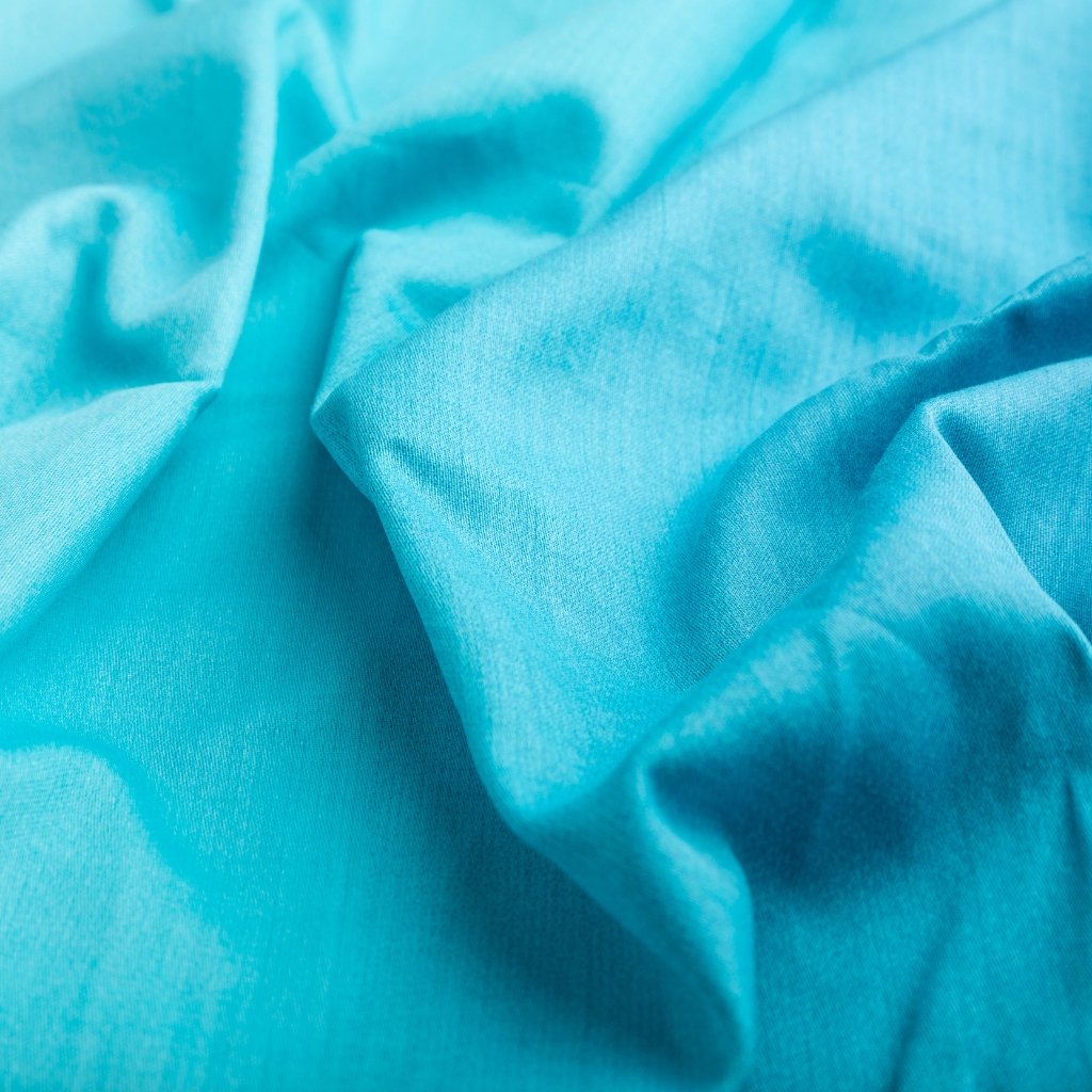 "Close-up view of light, airy blue cotton voile fabric with soft folds and a smooth, matte surface