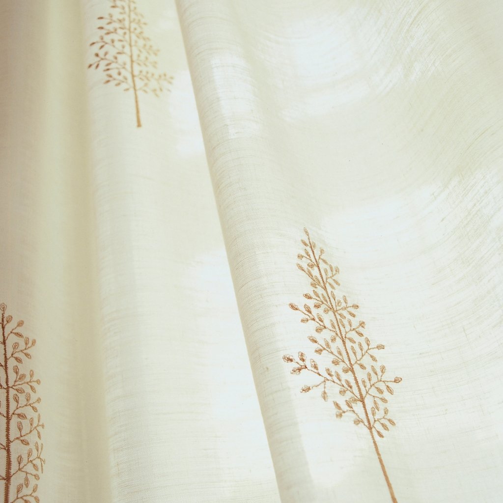 A close-up view of light cream cotton voile fabric with subtle sheer texture and delicate brown botanical embroidery of branching stems with tiny leaves.

